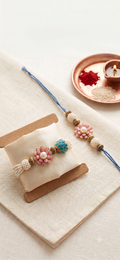 Handcrafted Aurora Pearl & Enamel Rakhi Set - Set of 2 matching rakhis for brother and sister, with intricate blue lotus bead and pink flowers. Gift-ready packaging and fast shipping within India.